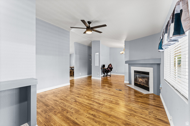Wood-finish flooring throughout, ceiling fan with integrated lighting, built-in fireplace, and window with blinds