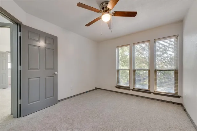 an empty room with chandelier fan and windows