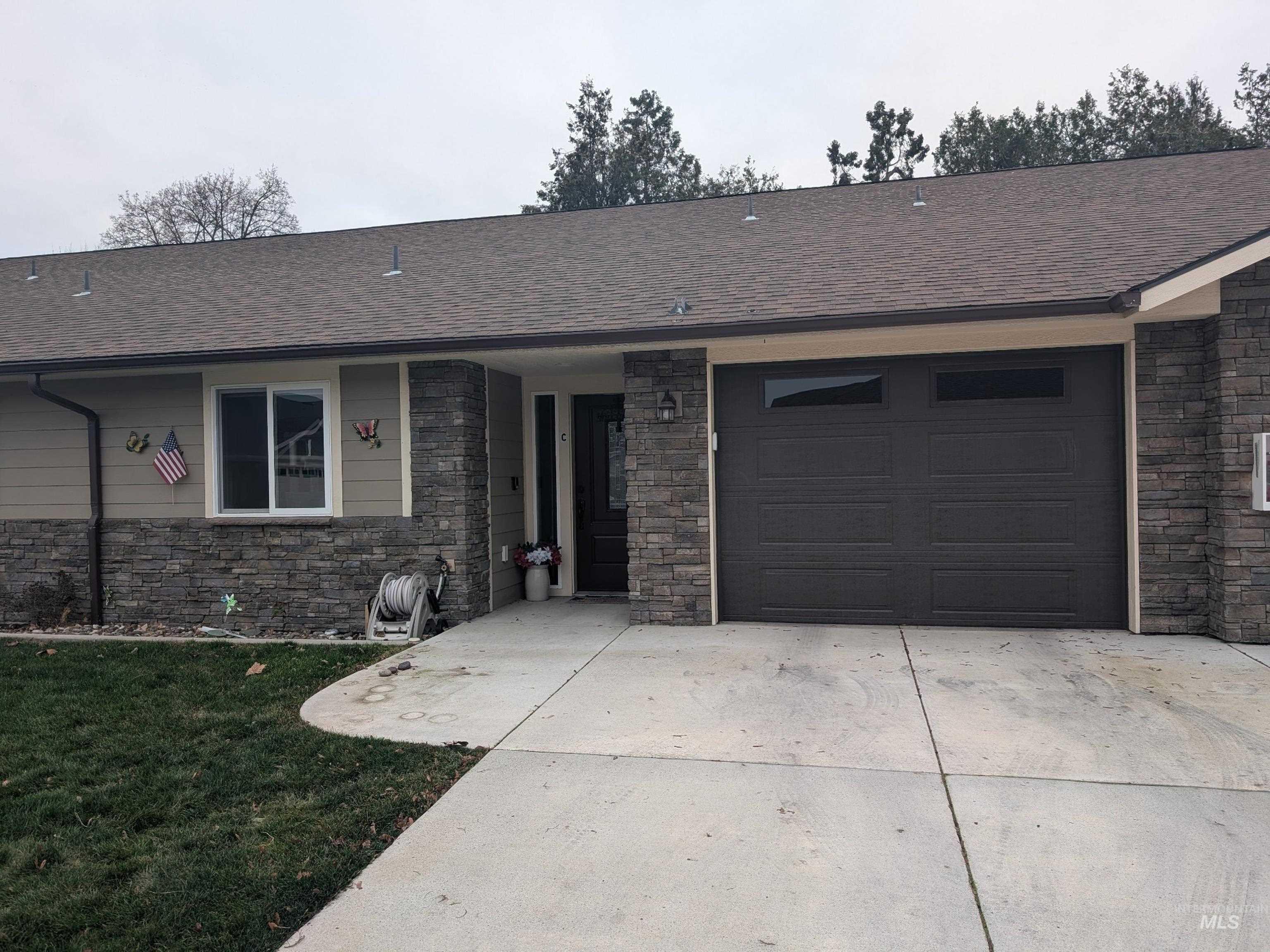 Ranch-style house featuring stone siding, roof with shingles, driveway, a front lawn, and a garage