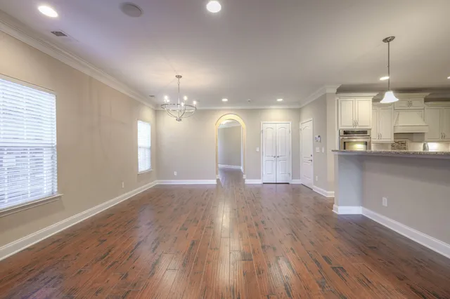 a view of an empty room and kitchen with wooden floor