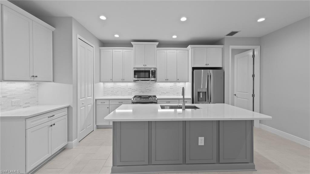 4636 Skysail Drive Naples, FL 34120 - Photo 7 of 46 a kitchen with kitchen island granite countertop a stove a sink a refrigerator and white cabinets