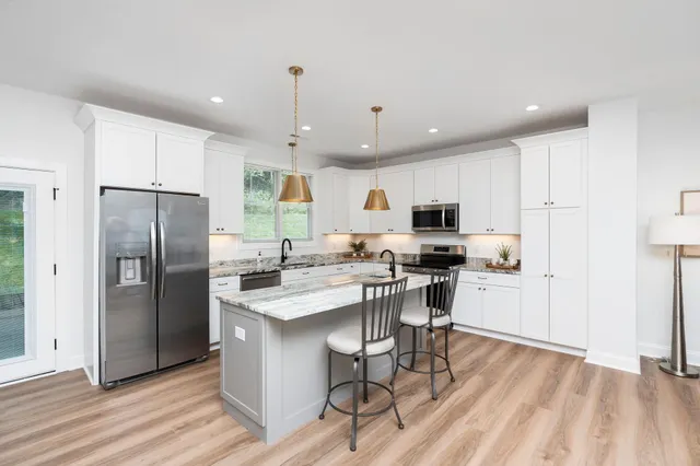 a kitchen with stainless steel appliances granite countertop a stove a sink dishwasher a refrigerator and a dining table with wooden floor