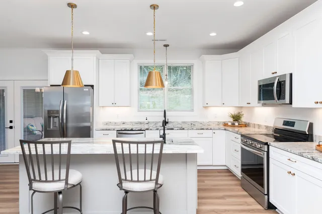 a kitchen with stainless steel appliances granite countertop a refrigerator a sink dishwasher a stove and white cabinets with wooden floor