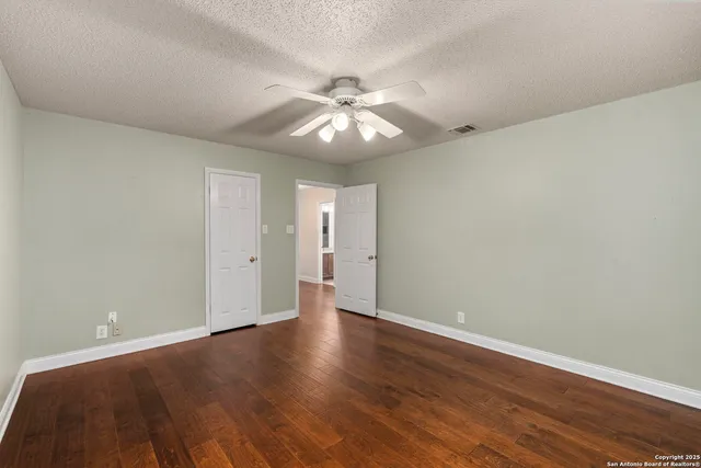 an empty room with wooden floor chandelier fan and windows