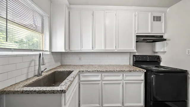 a kitchen with granite countertop a sink a stove and cabinets
