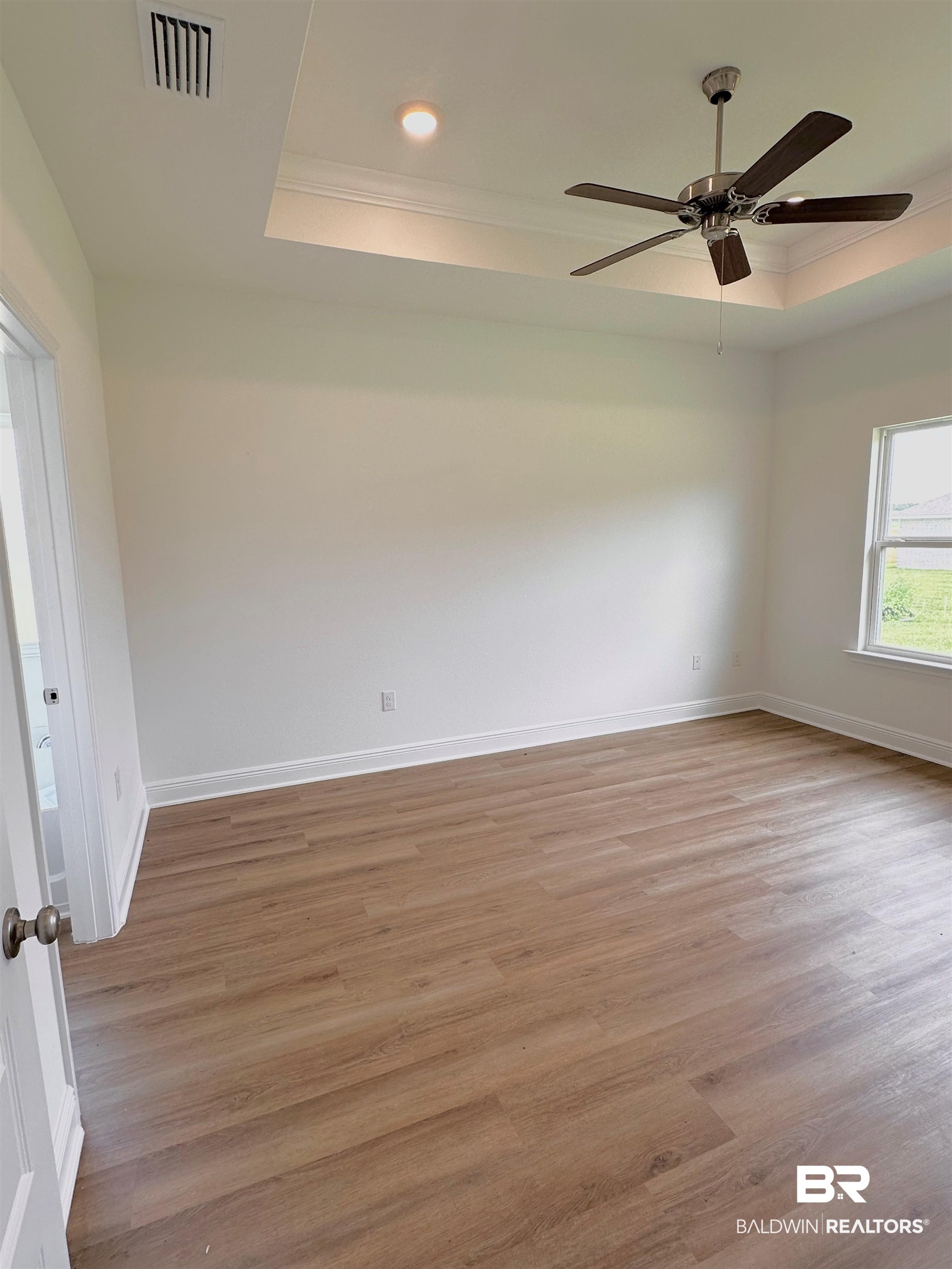 12946 Grand Rpds Road Fairhope, AL 36532 - Photo 9 of 19 Empty room with ceiling fan, light hardwood / wood-style floors, and a tray ceiling