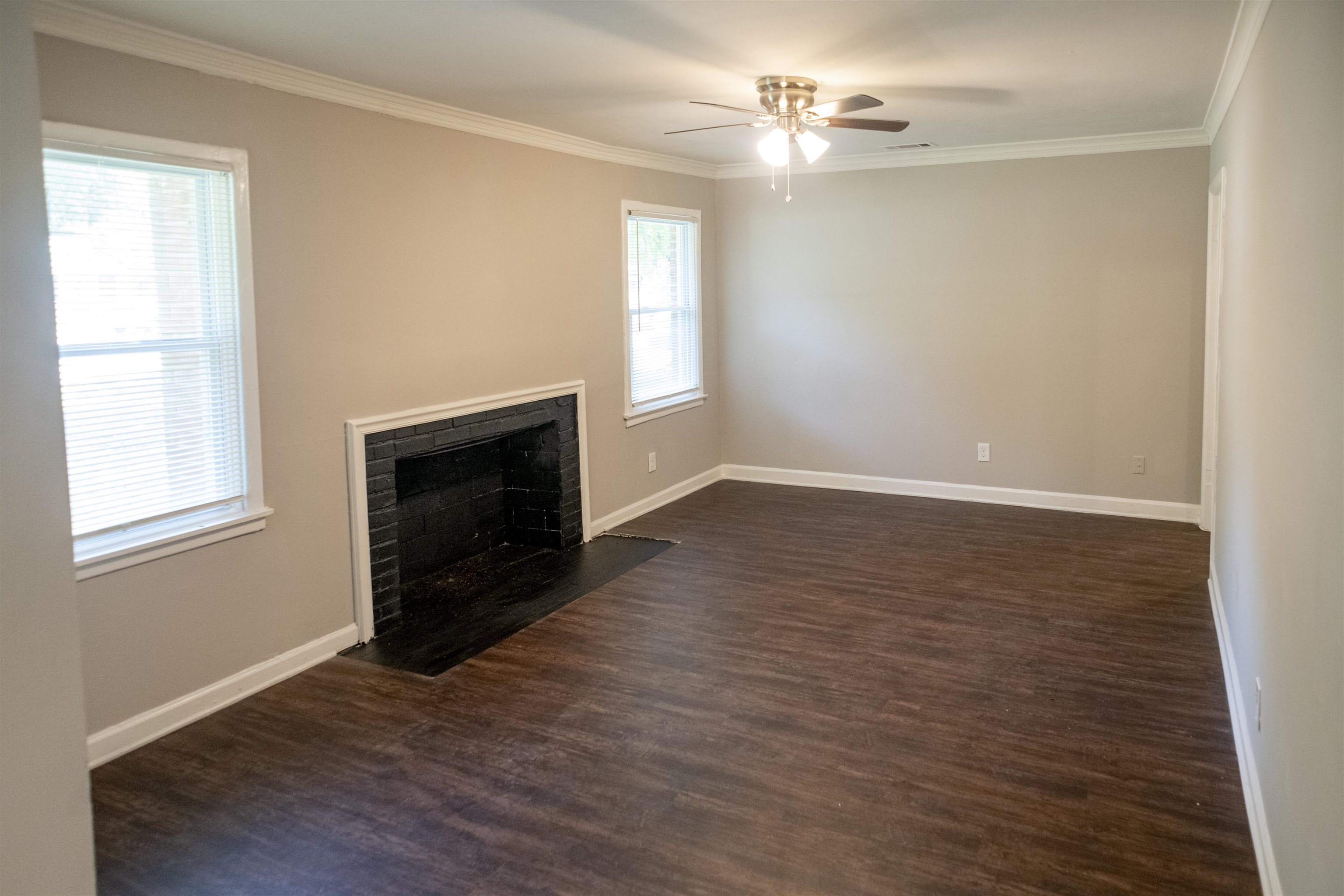 875 Enfield Road Memphis, TN 38116 - Photo 13 of 14 Spacious living room showcasing wood-finish flooring, a fireplace with dark surround, ceiling fan with integrated lighting, and abundant natural light from dual windows with blinds