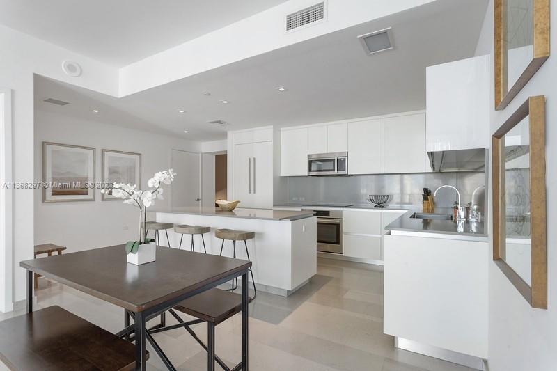 68 Southeast 6th Street, Unit 1209 Miami, FL 33131 - Photo 5 of 15 a kitchen with a table chairs microwave and cabinets