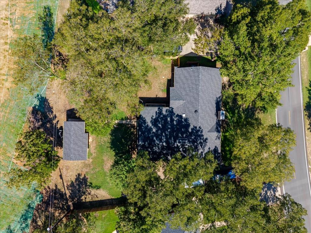 8105 Ravenswood Road Granbury, TX 76049 - Photo 27 of 28 Property featuring a main residence with a dark shingle roof, a detached ancillary structure with a dark shingle roof, and mature trees on the premises