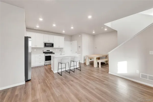 a kitchen with stainless steel appliances kitchen island granite countertop a stove a refrigerator a sink a dining table and chairs with wooden floor