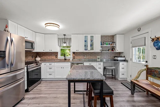 a kitchen with stainless steel appliances a stove a sink dishwasher a refrigerator white cabinets and wooden floor