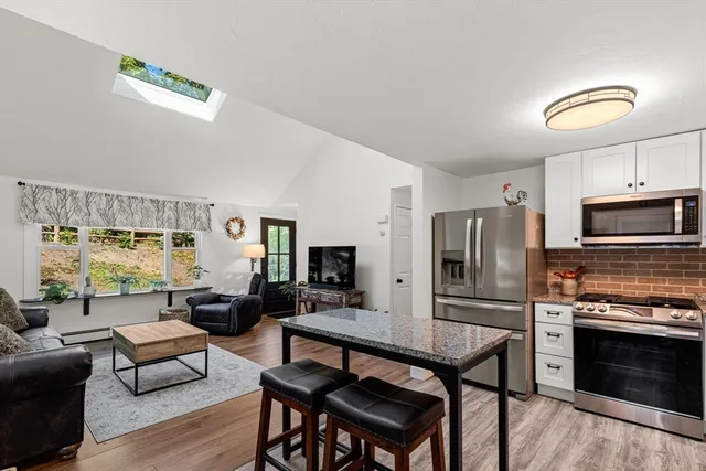 a living room with stainless steel appliances a dining table wooden floor and a large window