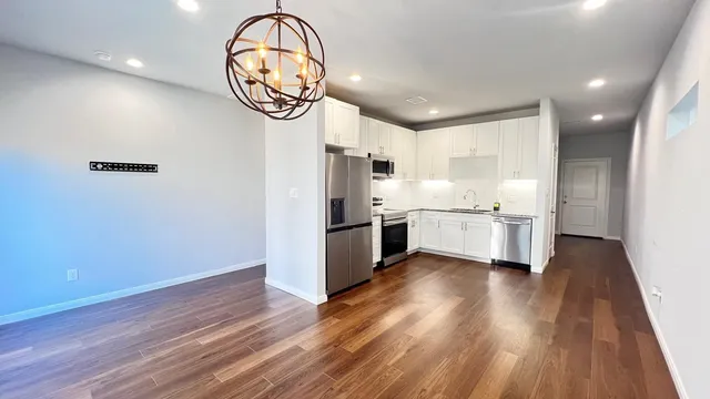 a kitchen with stainless steel appliances a refrigerator a oven a sink and white cabinets with wooden floor