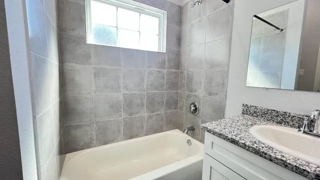 a bathroom with a granite countertop bathtub sink vanity and window