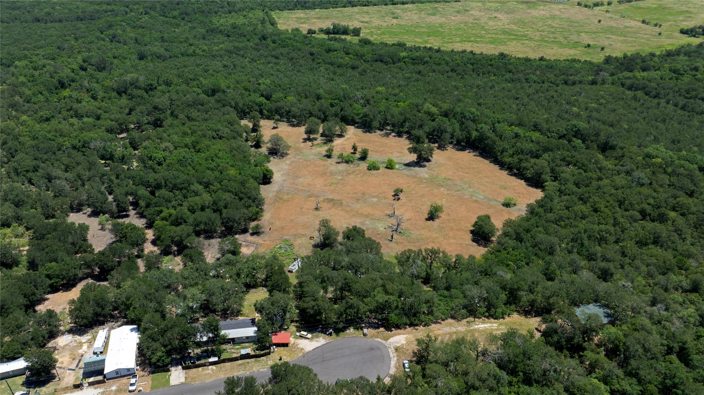 23318 Ingram Drive Elgin, TX 78621 - Photo 4 of 4 An expansive rural landscape showcasing natural clearings amidst abundant tree cover and surrounding neighborhood homes.