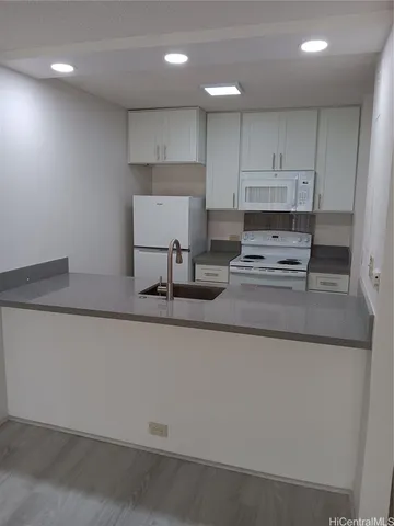 a kitchen with kitchen island granite countertop a sink a stove a refrigerator and white cabinets