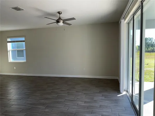 an empty room with wooden floor fan and windows
