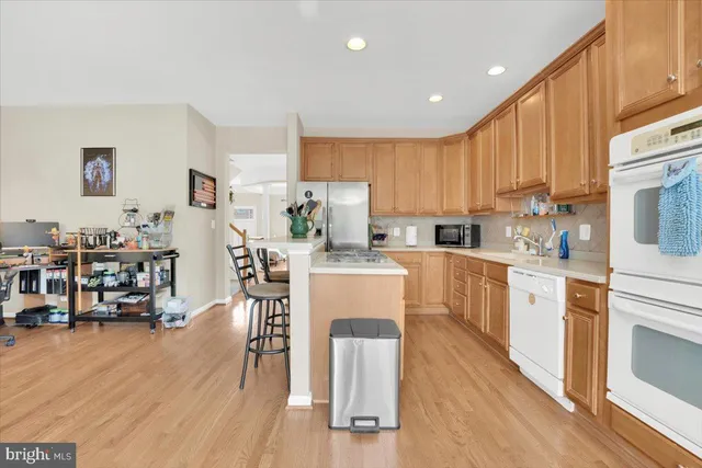 a kitchen with kitchen island wooden floors white appliances a center island and a refrigerator