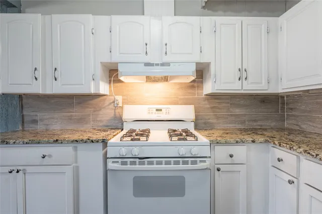 a kitchen with granite countertop white cabinets and white stove