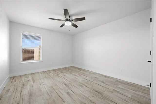 an empty room with wooden floor fan and windows