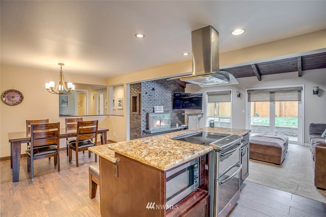 16120 Southeast 145th Place Renton, WA 98059 - Photo 7 of 22 a kitchen with stainless steel appliances granite countertop a stove top oven a dining table and chairs with wooden floor