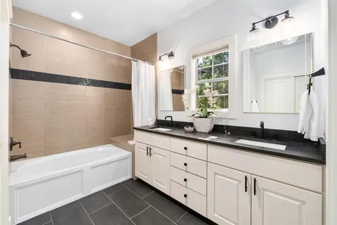 a bathroom with a granite countertop sink mirror bathtub and next to a window