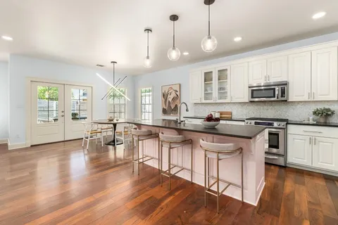 a kitchen with stainless steel appliances granite countertop a stove a sink dishwasher a refrigerator and white cabinets with wooden floor