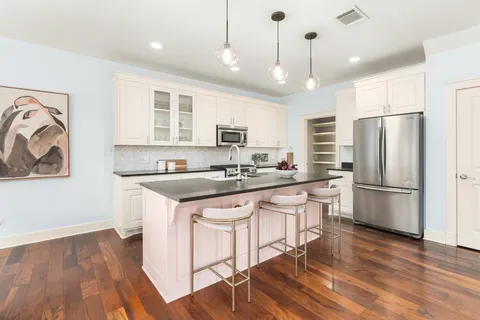 a kitchen with stainless steel appliances granite countertop a refrigerator a sink dishwasher a stove and white cabinets with wooden floor