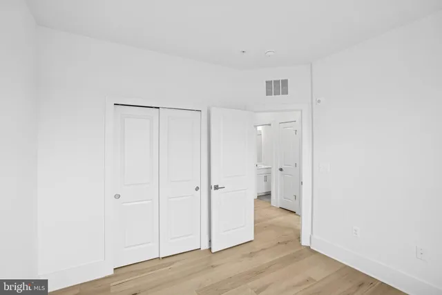 a view of an empty room with wooden floor and a bathroom