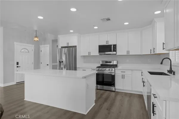a large kitchen with stainless steel appliances granite countertop a stove top oven a sink a refrigerator and white cabinets