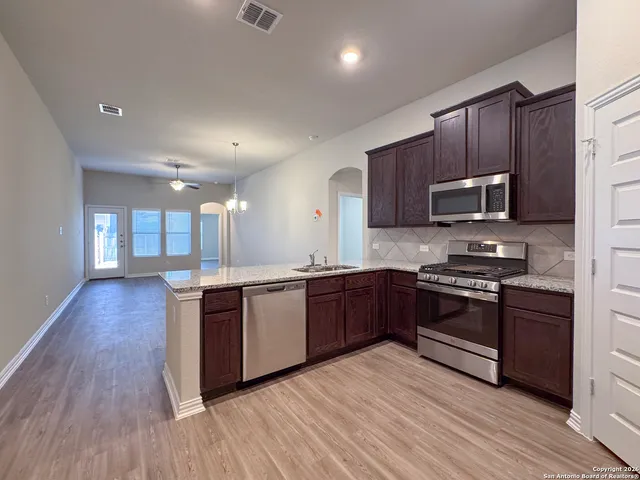 a view of an empty room with kitchen and a ceiling fan