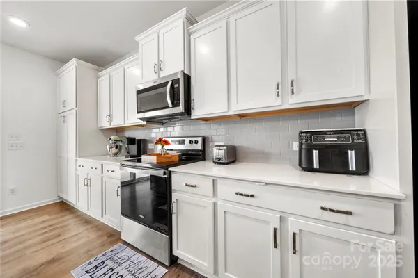 a kitchen with stainless steel appliances granite countertop white cabinets a sink a stove a microwave and wooden floors