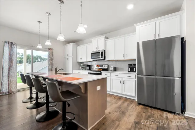 a kitchen with kitchen island a refrigerator a stove a sink and a dining table with wooden floor