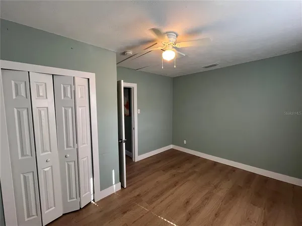 an empty room with wooden floor fan and windows