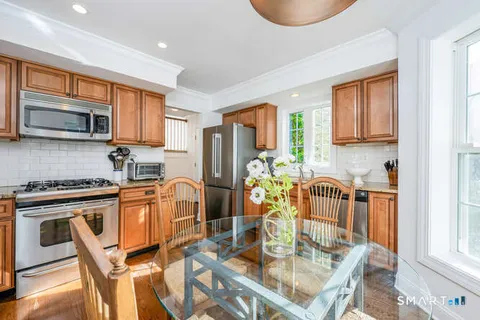 a kitchen with stainless steel appliances granite countertop a stove top oven a sink a dining table and chairs with wooden floor