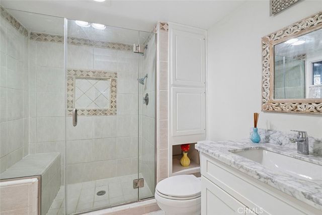 a bathroom with a granite countertop sink a mirror a shower and a toilet