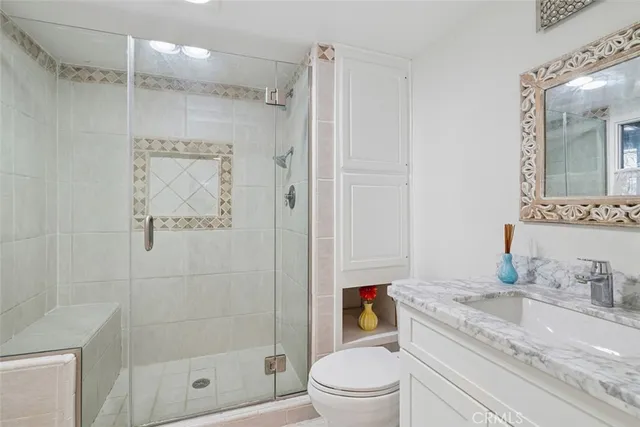 a bathroom with a granite countertop sink a mirror a shower and a toilet