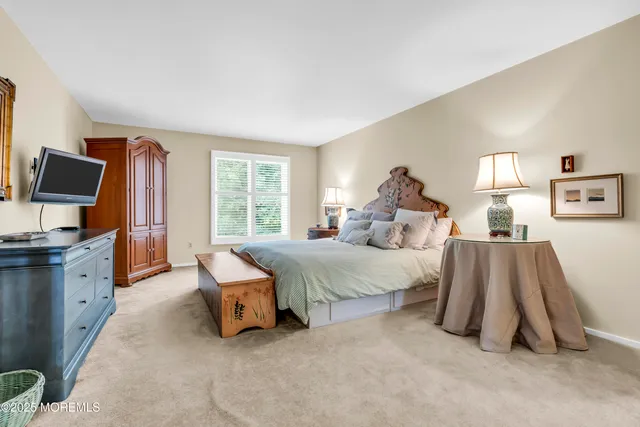 a spacious bedroom with a bed and a flat tv screen on dresser