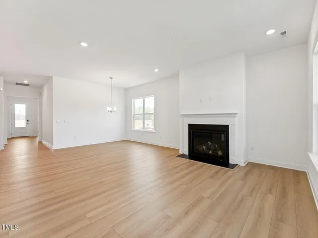 a view of an empty room with wooden floor fireplace and a window