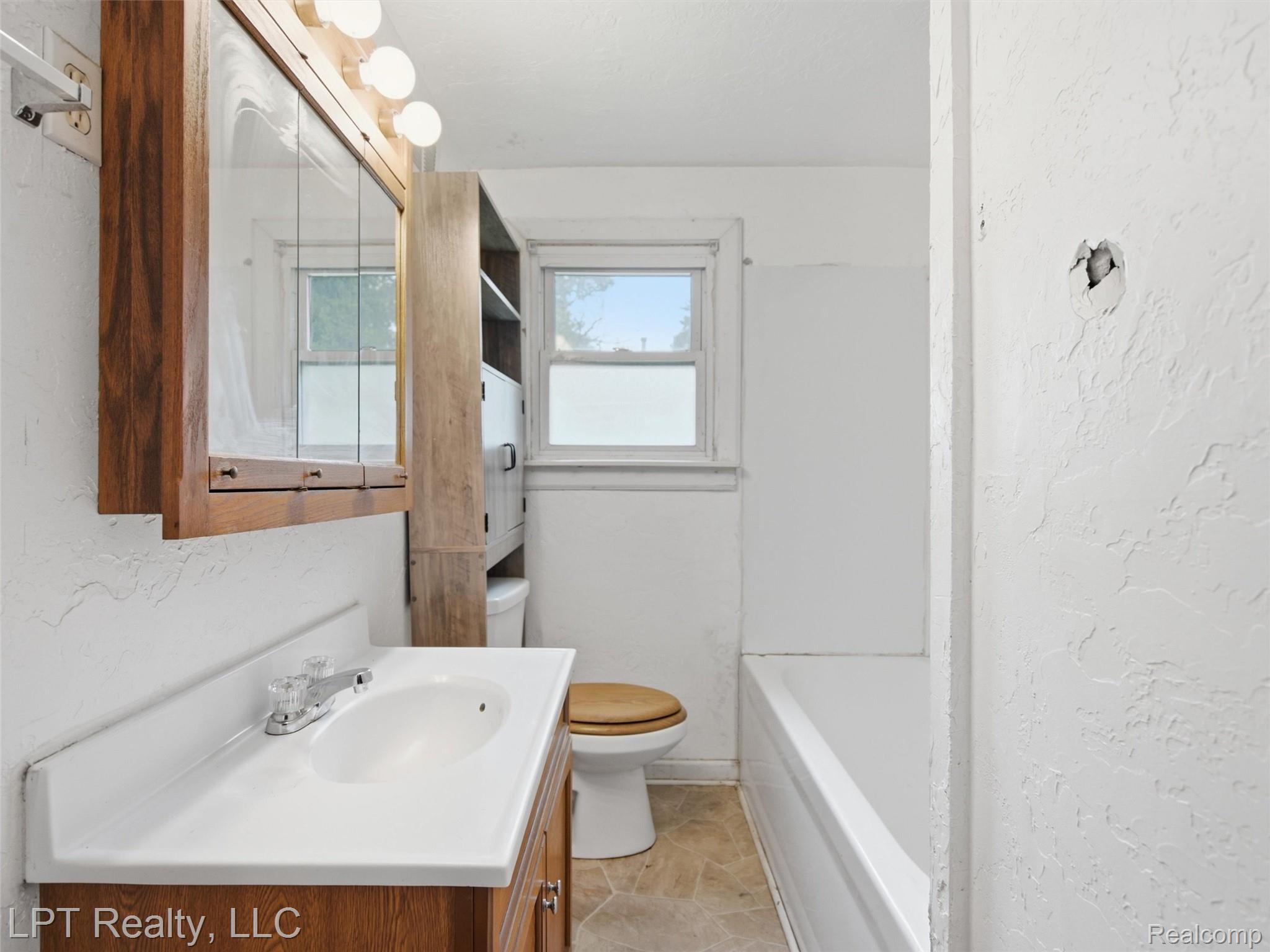 3385 North Genesee Road Flint, MI 48506 - Photo 9 of 24 White vanity with an integrated sink and chrome faucet, wood-finish medicine cabinet with mirrored doors, window with natural light, and a white bathtub