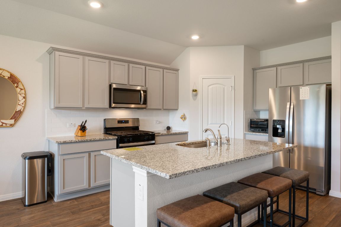 13908 Mamie Eisenhower Road Manor, TX 78653 - Photo 8 of 23 a kitchen with granite countertop a stove a sink a refrigerator and wooden cabinets