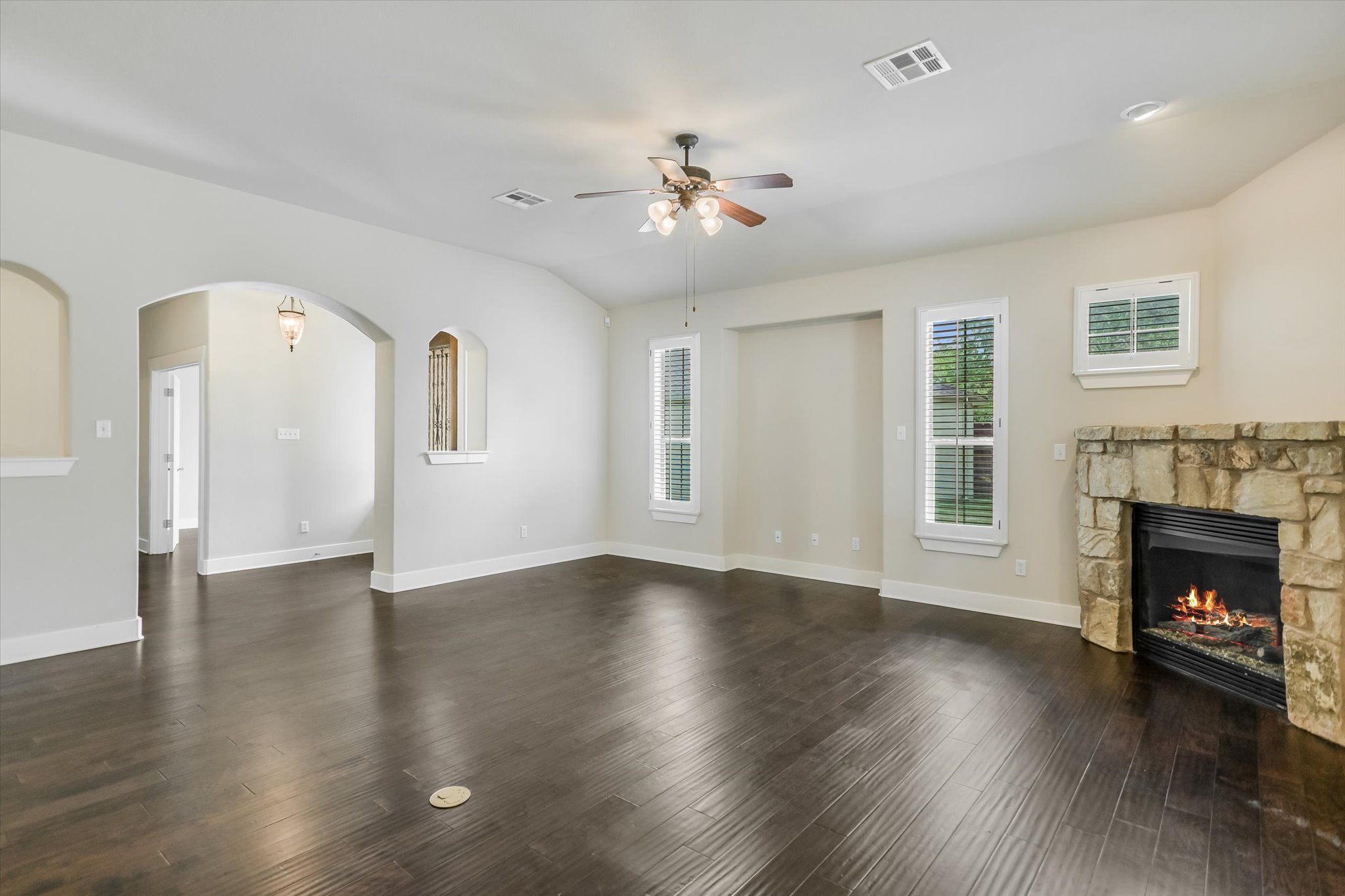 210 Rivulet Lane Austin, TX 78738 - Photo 6 of 20 Unfurnished living room with arched walkways, dark wood finished floors, a fireplace, and ceiling fan