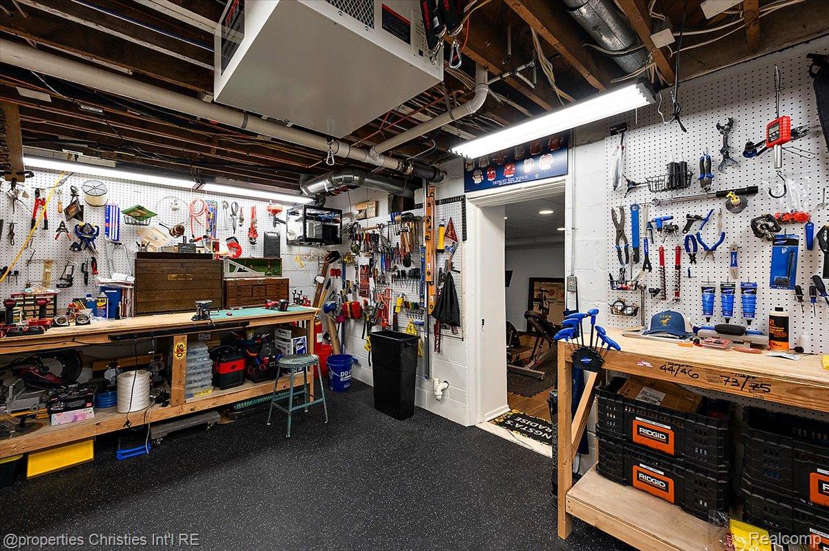 528 Covington Road Bloomfield Hills, MI 48301 - Photo 58 of 75 Dedicated workshop space featuring extensive pegboard organization systems, durable rubber flooring, exposed ceiling joists, overhead fluorescent lighting, and a substantial built-in workbench