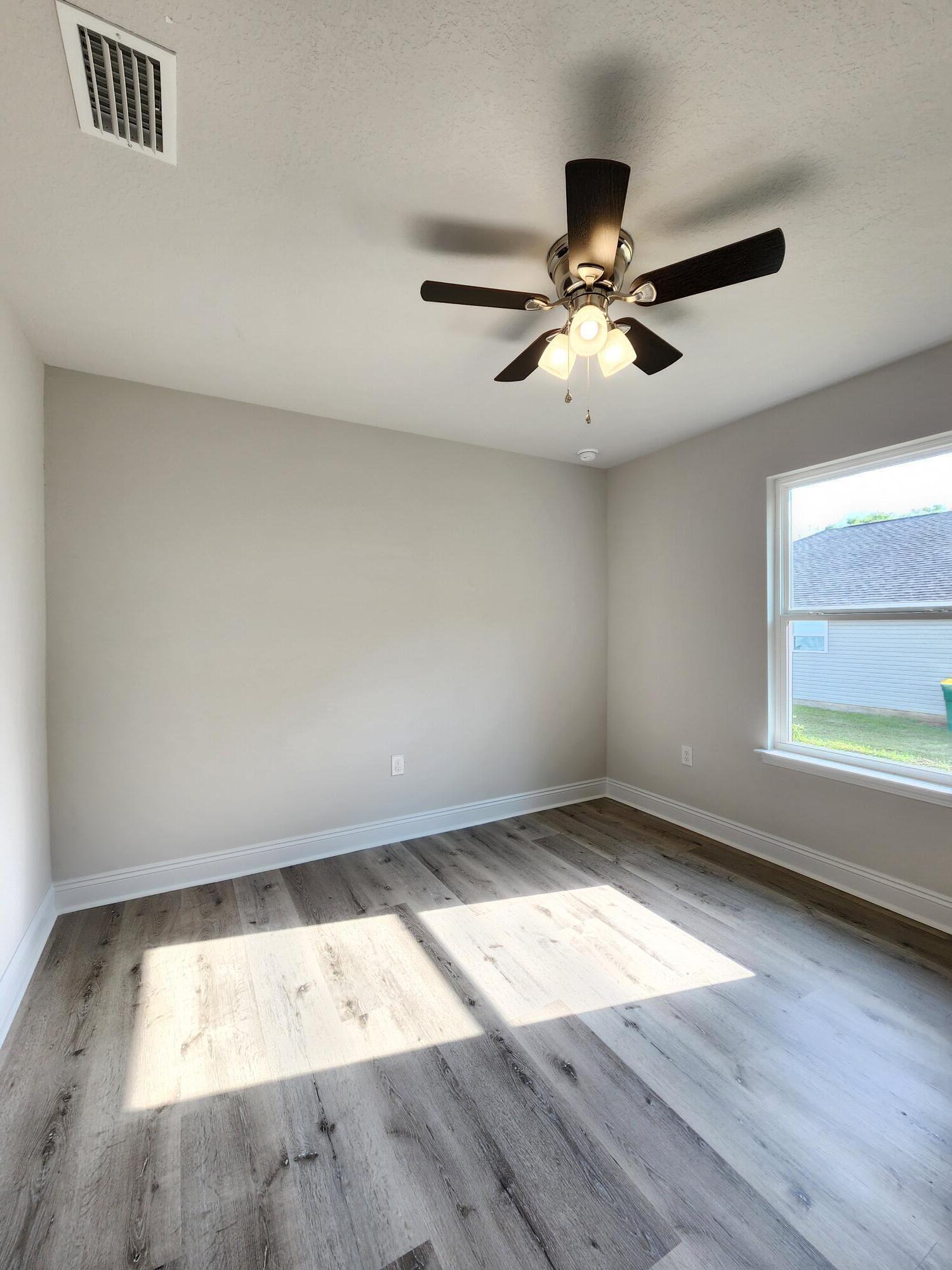 3168 Main Street Crestview, FL 32539 - Photo 17 of 18 an empty room with wooden floor chandelier fan and windows