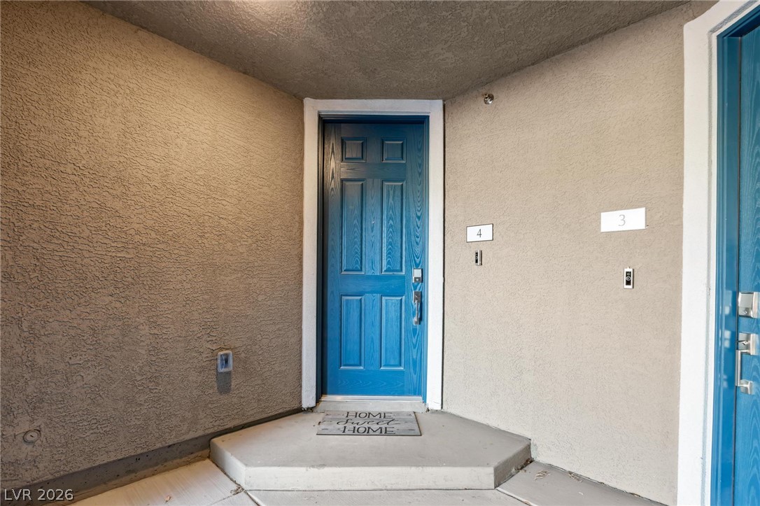7310 North Decatur Boulevard, Unit 4 North Las Vegas, NV 89084 - Photo 26 of 35 A vibrant blue entry door welcomes residents to unit number 4, set against textured stucco walls.