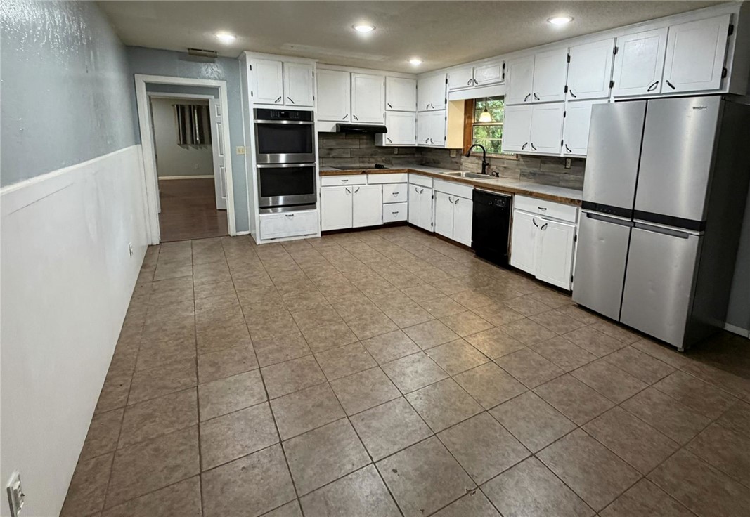 Kitchen featuring extensive white cabinetry, tile flooring, stainless steel double ovens, stainless steel refrigerator, and a dark sink with a gooseneck faucet