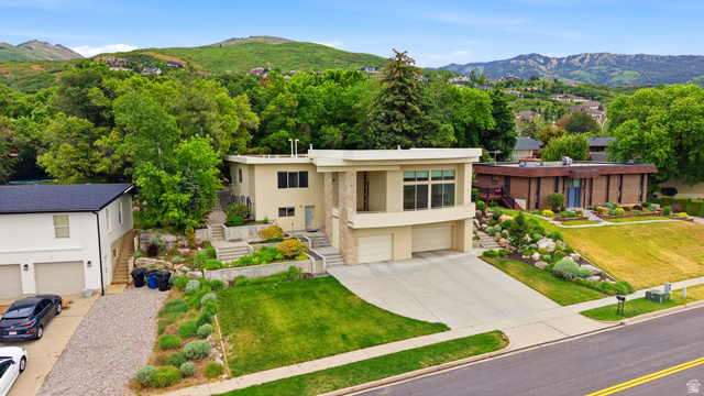1389 Millbrook Way Bountiful, UT 84010 - Photo 4 of 74 Contemporary architecture featuring a stucco and stone exterior, multi-level landscaping with mature plantings, an integrated two-car garage, and a concrete driveway