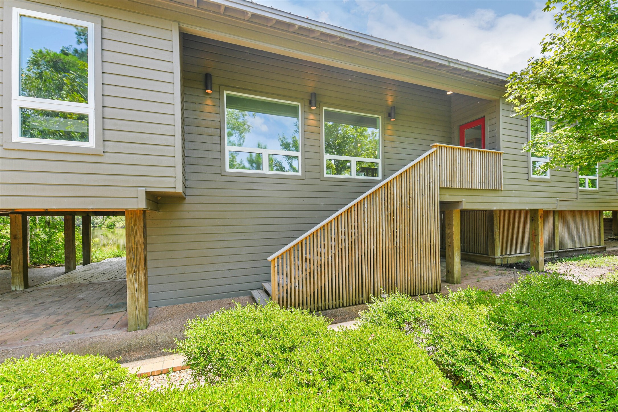 88 Raccoon Ramble Cleveland, TX 77327 - Photo 6 of 43 Elevated home with sleek horizontal siding, large windows for natural light, and a welcoming red door. A wooden staircase leads to the main entrance, surrounded by lush greenery.
