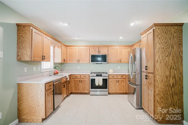 a kitchen with stainless steel appliances granite countertop a stove top oven a sink a refrigerator and white cabinets with wooden floor