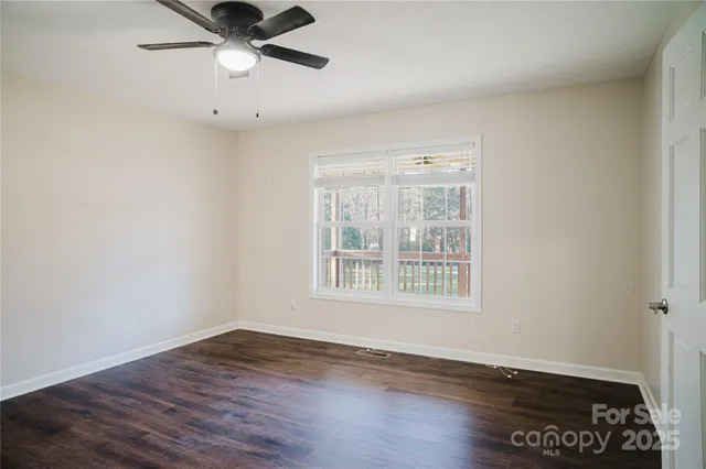 an empty room with wooden floor fan and windows